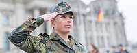Eine Soldatin im Tarnanzug steht vor dem Bundestagsgebäude in Berlin und grüßt militärisch..