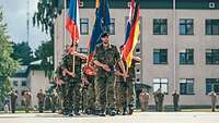 Soldaten marschieren mit Flaggen unterschiedlicher Nationen auf einem Platz.