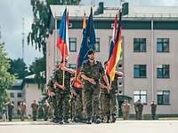 EFP Kommandowechsel Soldaten marschieren mit Flaggen unterschiedlicher Nationen auf einem Platz.