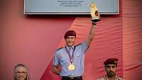 Siegerehrung: Der junge Sportsoldat hält seine Trophäe in die Höhe. Zwei Personen stehen unten im Bild.