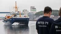 Zwei Menschen warten im Hafen auf das gerade einlaufende Schiff