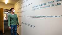 Eine Person schaut auf eine weiße Wand mit Schrift.