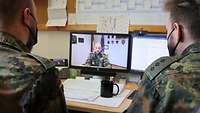 Zwei Soldaten sitzen am Schreibtisch vor einem Laptop und schauen sich ein Video an.