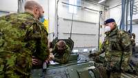In einer Halle stehen mehrere Soldaten auf einem Panzer und sprechen miteinander.