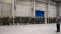In einer Halle stehen Soldaten in Formation angetreten. Ein General steht vor der Formation.