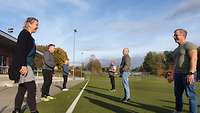 Soldaten in sportlicher Kleidung stehen auf einem Sportplatz und werfen sich kleine Bälle mit verschiedenen Händen zu.