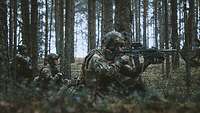 Mehrere Soldaten hocken mit ihren Waffen im Anschlag in einem Wald.