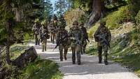 Eine Gruppe von Soldaten laufen mit Waffen einen Weg im Gebirge entlang.