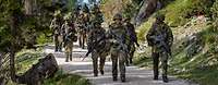 Eine Gruppe von Soldaten laufen mit Waffen einen Weg im Gebirge entlang.
