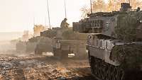 Mehrere Panzer fahren hintereinander über verschlammtes Gefechtsgelände.