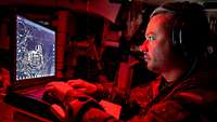 Ein Soldat sitzt in einem militärischen Fahrzeug und arbeitet an einem Computer.