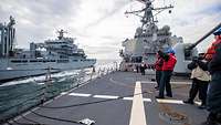 Blick auf das Vorschiff eines Kriegsschiff; darauf stehen mehrere Marinesoldaten mit Schutzhelmen.