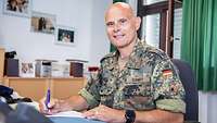 Ein Soldat sitzt an einen Schreibtisch und blickt in die Kamera