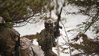 Zwei Soldaten bewegen sich auf einem Felsen mit dem Gewehr im bewaldeten Gebirge.