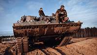 Zwei Soldaten sitzen auf einem Bergepanzer und schauen nach rechts