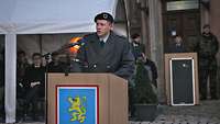 Ein Soldat steht im Freien an einem Pult und hält eine Rede.