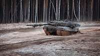 Ein Kampfpanzer fährt von rechts nach links auf sandigem Untergrund