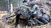 Zwei Soldaten knien mit ihren Waffen neben einem Erdhügel.