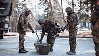 Erste Station erreicht Zwei Soldaten in ABC-Schutzausstattung legen unter Anweisung eines dritten Soldaten ihre Ausrüstung in Kisten