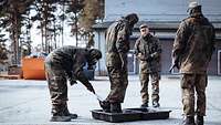 Ein Soldat steht in einer Plastikwanne. Ein zweiter Soldat reinigt seine Schutzstiefel mit einer Bürste. 