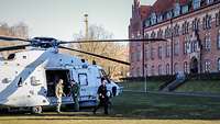 Ein Admiral in dunkelblauer Uniform geht über einen Rasen; im Hintergrund ein hellgrauer Hubschrauber.