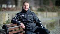 Eine Frau in Sportkleidung sitzt auf einer Bank im Freien