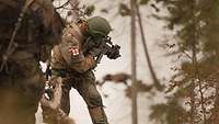 Ein Soldat schießt mit dem Gewehr von einem Felsen aus in den verschneiten Wald.