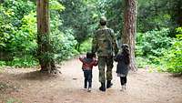 Ein Soldat geht mit zwei Kinder im Wald spazieren.