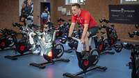 Ein Mann in Sportkleidung fährt auf einem Heimtrainer in einer Sporthalle.