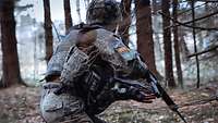 Ein deutscher Soldat läuft mit seinem Gewehr durch ein bewaldetes Gebiet 
