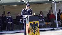 Oberst Springer hält eine Rede Ein Soldat steht auf einem Platz hinter einem Pult und hält eine Rede.