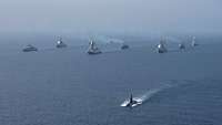 Mehrere Kriegsschiffe fahren in Formation durch das Meer.