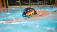 Ein Mann schwimmt mit Deutschland-Badekappe in einem Schwimmbecken.