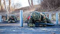 Zwei Soldaten mit ihren Waffen kriechen unter einem Drahthindernis hindurch.