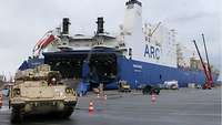Anlandung des Materials Ein Panzer fährt aus einem Schiff heraus, dass Schiff ist in voller Länge im Hintergrund zu sehen.