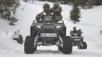 Vier Soldaten fahren mit zwei Quads auf einem verschneiten Weg.