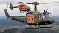 Zwei Hubschrauber mit jeweils den Buchstaben SAR auf orangefarbenem Grund fliegen nebeneinander her.
