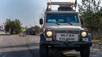 Ein Geländewagen mit Schild ,,Militaer Kolonne" fährt vor Militärfahrzeugen auf einer Straße