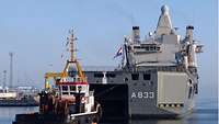 Ein großes Militärschiff mit Schlepper in einem Hafenbecken