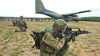 Zivilisten besteigen ein Flugzeug. Soldaten sichern die Umgebung.