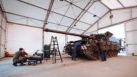 Vier Soldaten arbeiten in einem Wartungszelt an einer Panzerhaubitze