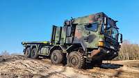 Geschütztes Wechselladersystem WLS der Bundeswehr im Gelände Ein grün-brauner LKW steht auf einem Sandberg vor blauen Himmel