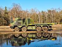 Geschütztes Wechselladersystem WLS der Bundeswehr Geländefahrt Ein grün-brauner LKW steht vor einem Teich im Gelände. Im Hintergrund stehen Bäume