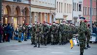Soldaten marschieren eine Straße entlang. Trommler, Fackelträger und Zuschauer stehen am Rand.