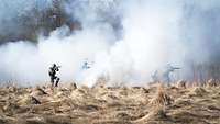 Bewaffnete Soldaten bewegen sich durch die vom Nebel der Nebelgranaten eingehüllte Landschaft.