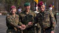 Drei Soldaten stehen nebeneinander auf einem Platz und reichen sich die Hände zur Mitte.