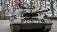Drei Soldaten fahren in einem Panzer. Ein Soldat grüßt militärisch.