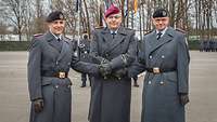 Drei Soldaten im Dienstanzug stehen nebeneinander und reichen sich auf einem Appellplatz die Hände.