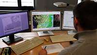 Der Wetterberater an seinem Schreibtisch, vor ihm drei Monitore mit Wetterdaten 