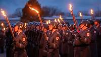 Zahlreiche Soldaten stehen in der Dämmerung mit Fackeln und Gewehren in Reihen nebeneinander.